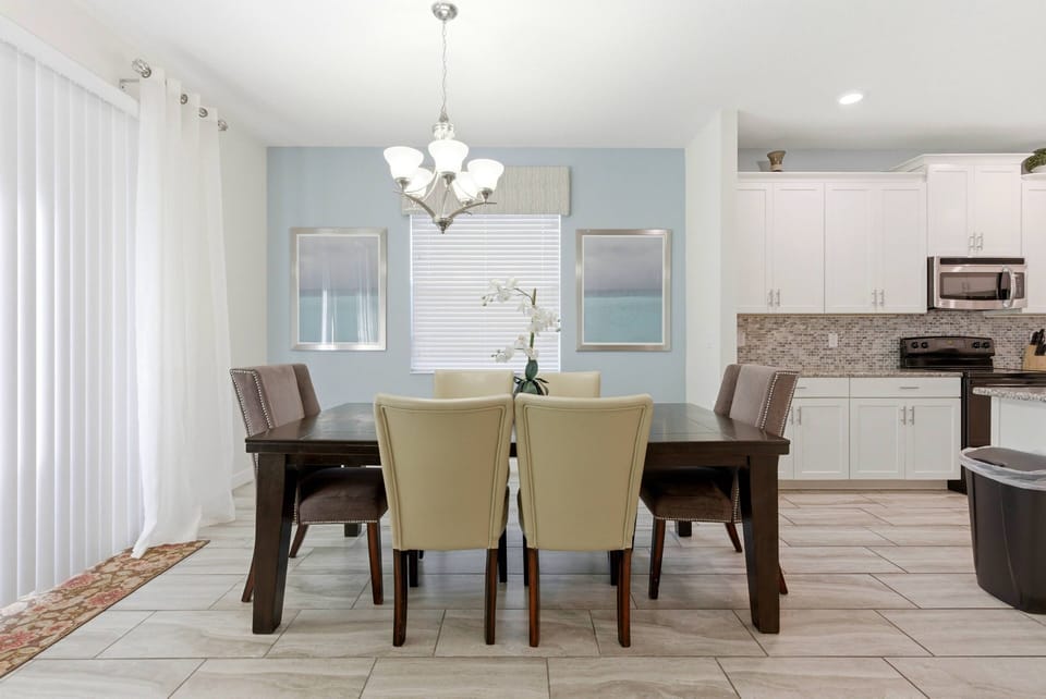 This bright dining area features a spacious dark wood table with cream and gray upholstered chairs, perfect for family meals. Large windows let in natural light, enhancing the modern decor and creating a warm, inviting atmosphere.