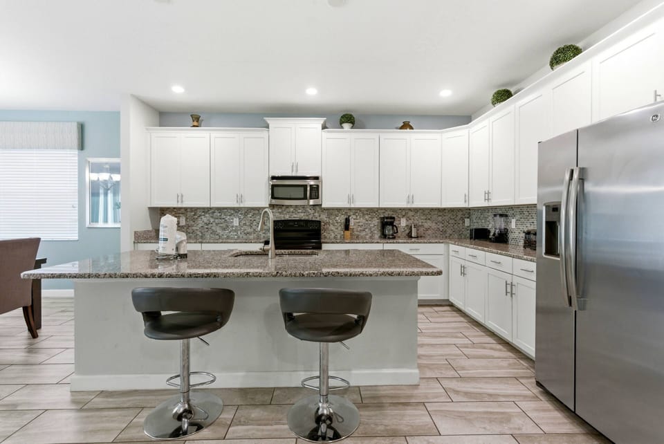 Welcome to this inviting kitchen with sleek white cabinetry and stunning granite countertops, ideal for your culinary adventures. Modern stainless-steel appliances and chic bar stools create a stylish space for everyone to enjoy.