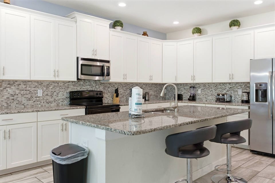 This modern kitchen boasts sleek white cabinetry and a spacious granite island, ideal for casual meals or morning coffee. Stylish bar stools encourage conversation, while the elegant backsplash adds a sophisticated touch.