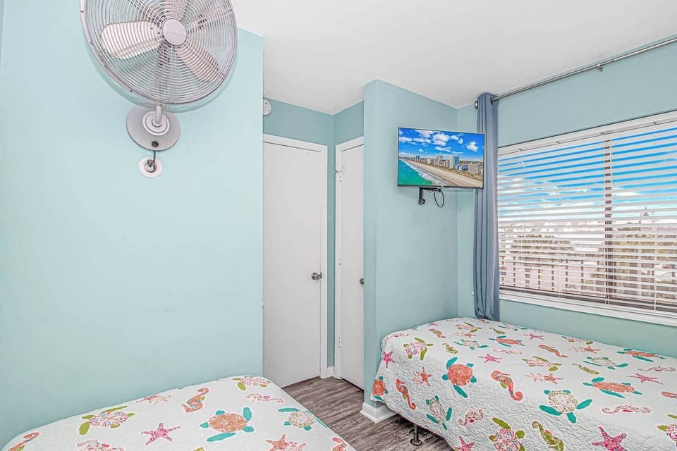 Bright third bedroom with smart TV and mounted fan. 