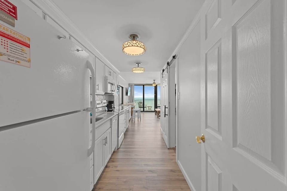 Bright, coastal-inspired galley kitchen with crisp white cabinetry, modern appliances, and a straight sightline to your oceanfront balcony. ✨