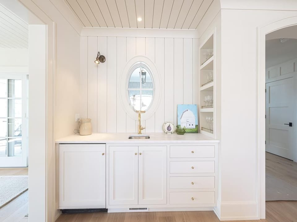 Charming wet bar area with a round mirror and open shelving, perfect for entertaining guests in this coastal home.