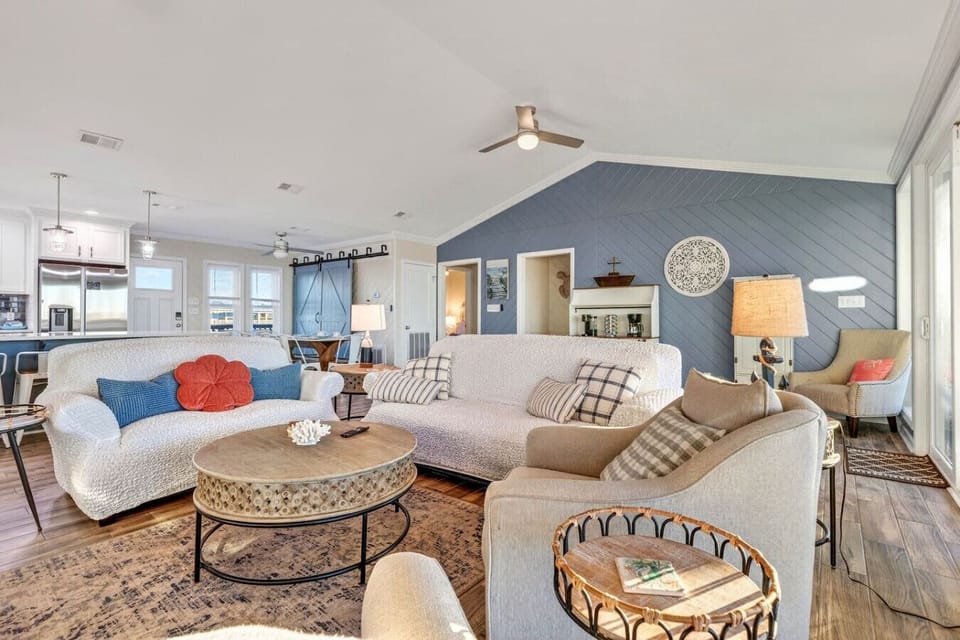 This spacious open-concept living room features multiple seating areas, stunning water views, and a stylish blue accent wall perfect for relaxing with family.