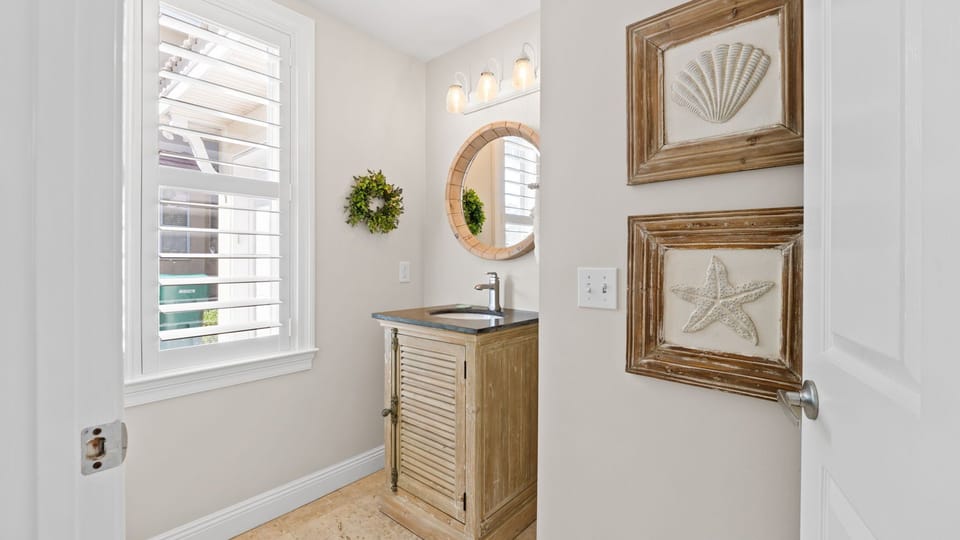 Bright half bath featuring a rustic wood vanity, stone countertop, round mirror, and beach-inspired décor.