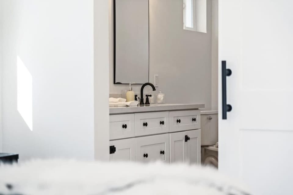 Bright and serene primary bedroom featuring a plush king bed, modern furnishings, French doors to the backyard, and a private en-suite bathroom.