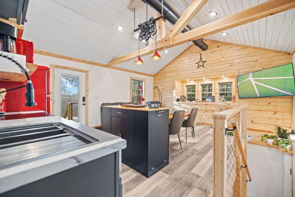 Open-concept cabin living space with vaulted ceilings, full kitchen, dining area, and smart TV.