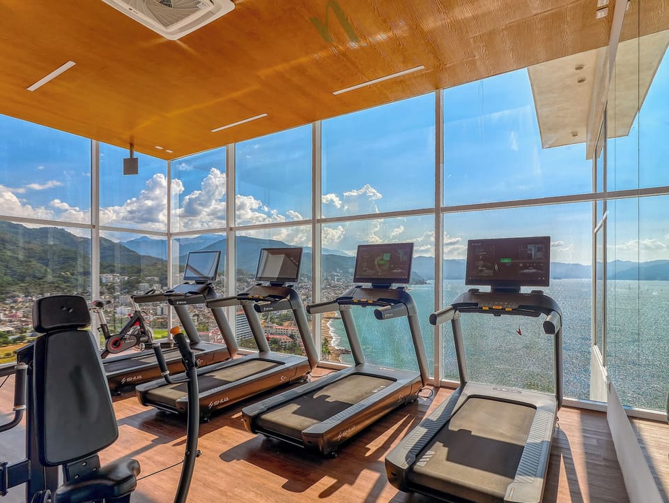 Modern fitness center with cardio equipment and floor-to-ceiling windows showcasing stunning ocean and coastline views.