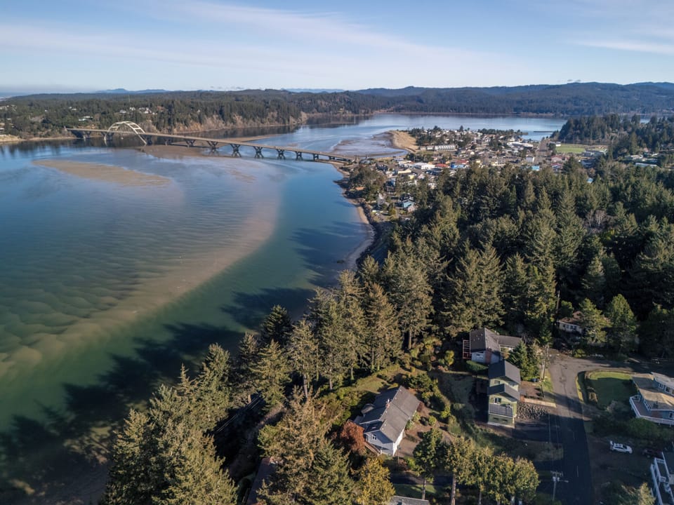 Stunning aerial perspective showcasing the coastal town, iconic bridge, and forested waterfront setting of this peaceful retreat destination.