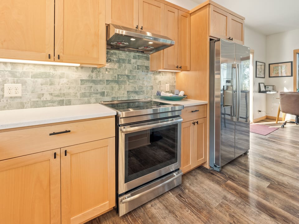 Your gourmet kitchen features gleaming stainless steel appliances, warm wood cabinetry, and stone backsplash for memorable home-cooked meals.