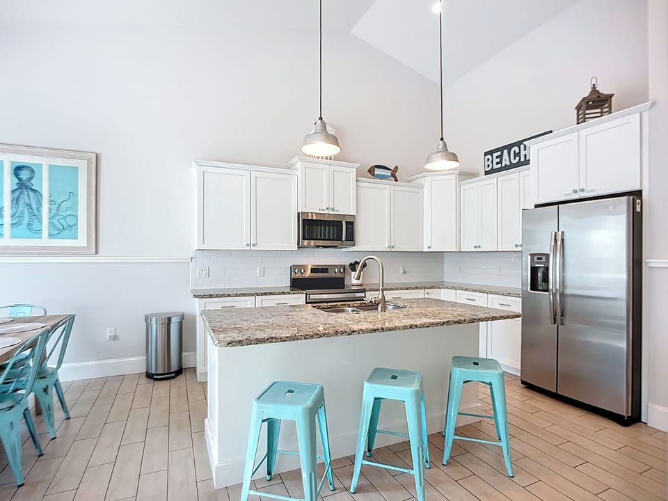 Your coastal kitchen features crisp white cabinets, granite countertops, and charming turquoise stools perfect for morning coffee or meal prep.