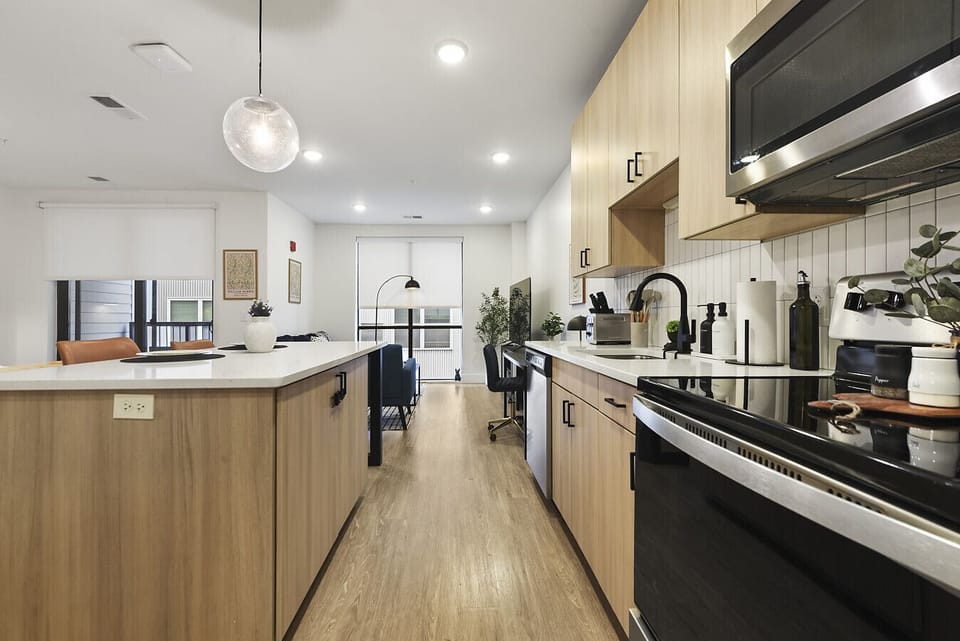 Stunning modern kitchen featuring light wood cabinetry, sleek black countertops, stainless steel appliances, and a large island – perfect for cooking and entertaining in this bright apartment.