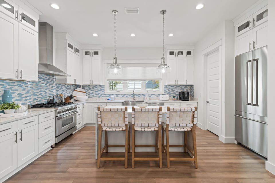 Gather around this stunning kitchen island where crisp white cabinetry meets coastal charm through beautiful blue mosaic backsplash tiles.