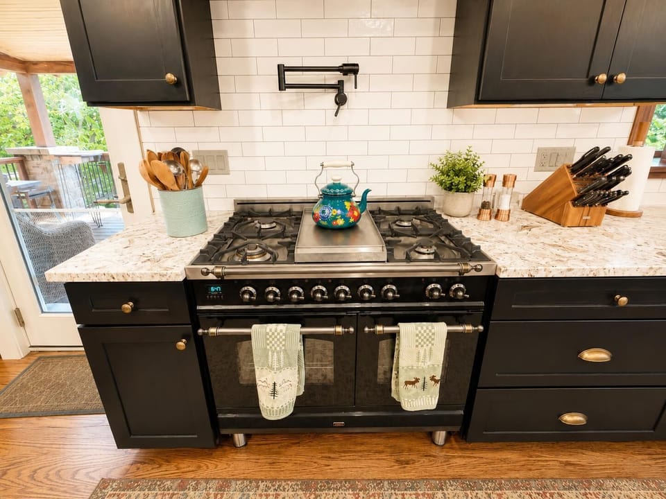 Black gas range with double oven sits between granite countertops and white subway tile backsplash.