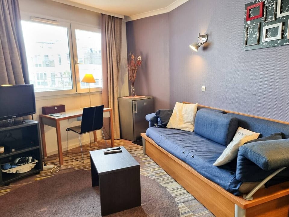 Salon avec canapé lit, coin TV, Box wifi, coin bureau, table basse et réfrigérateur.