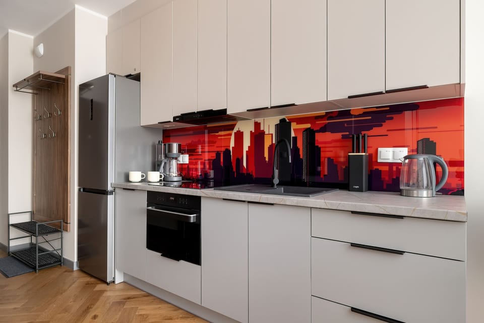 The functional kitchen includes a silver refrigerator and a black built-in oven. The illuminated red panel gives the space a dynamic, modern character.