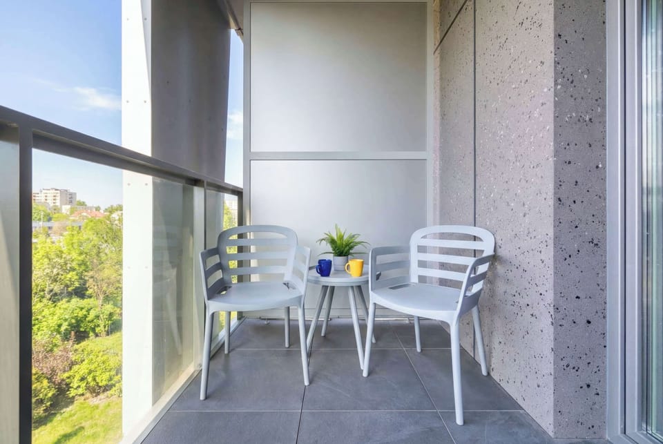 A private balcony provides a peaceful retreat with two white chairs and a small table. It overlooks lush greenery, perfect for a quiet morning coffee.
