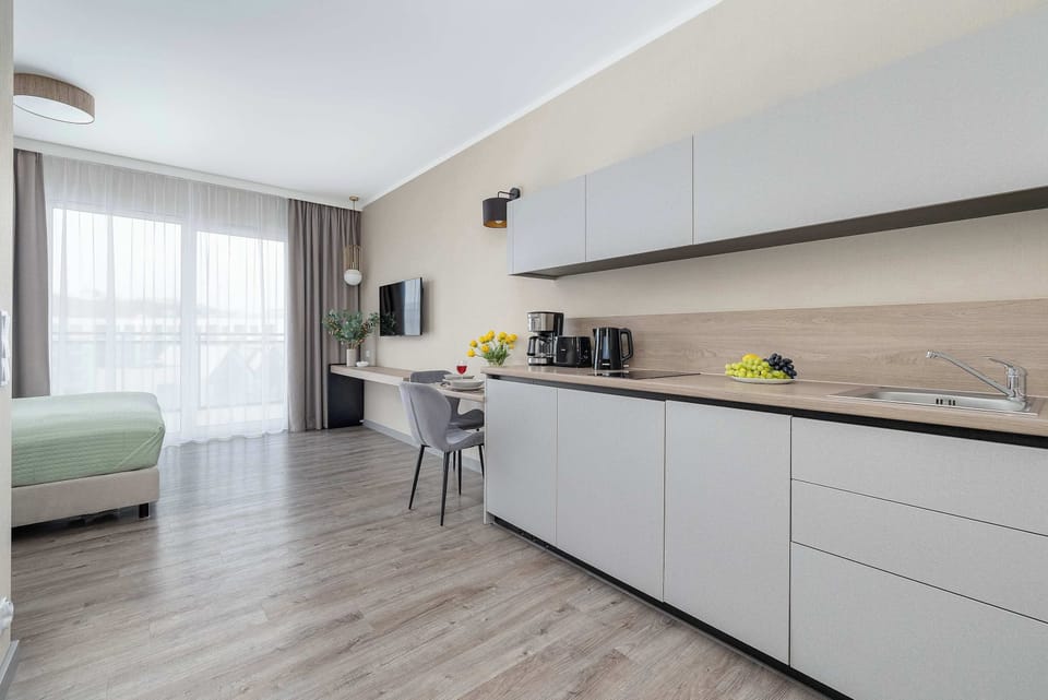 A sleek, fully equipped kitchenette with white cabinets, a stove, and a dining area. The minimalist design creates a bright and airy atmosphere.