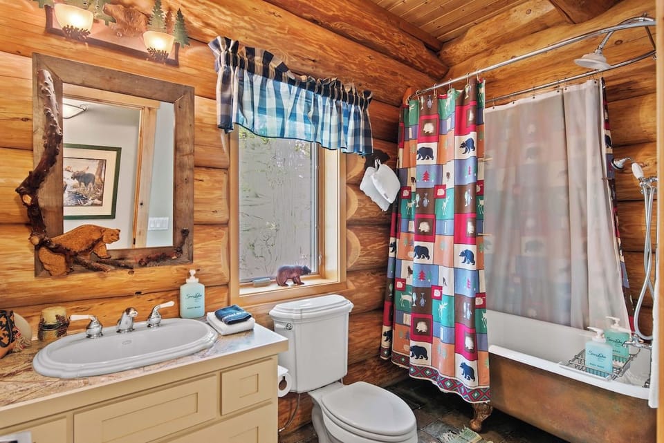 Step into your private cabin bathroom, where rustic wood walls and playful bear-patterned details create a warm, mountain retreat. The shower curtain's cheerful design and handcrafted mirror welcome you after a day of adventure.