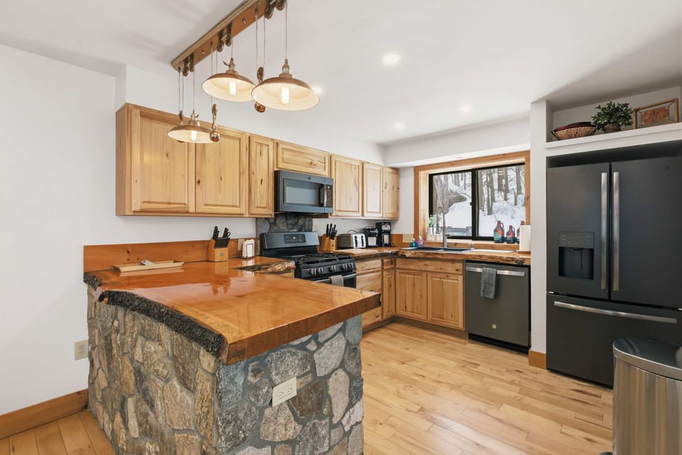 Fully equipped kitchen with stainless steel appliances, live-edge wood countertops, and a stone-accented island—ready for everything from quick breakfasts to family dinners.