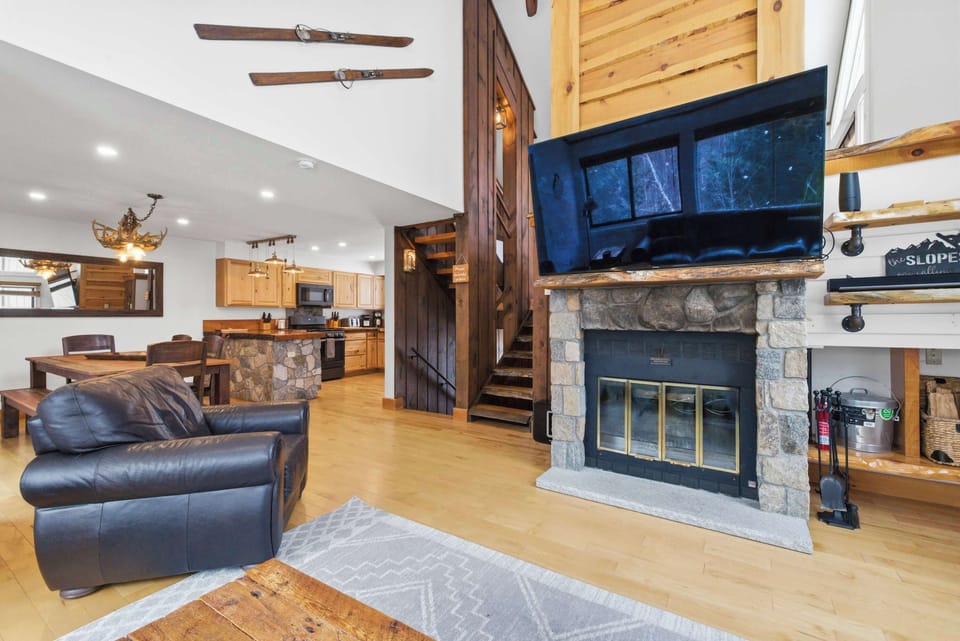 Relax in the open-concept living area featuring a floor-to-ceiling stone fireplace, oversized sectional, and 75" TV—perfect for cozy mountain evenings.