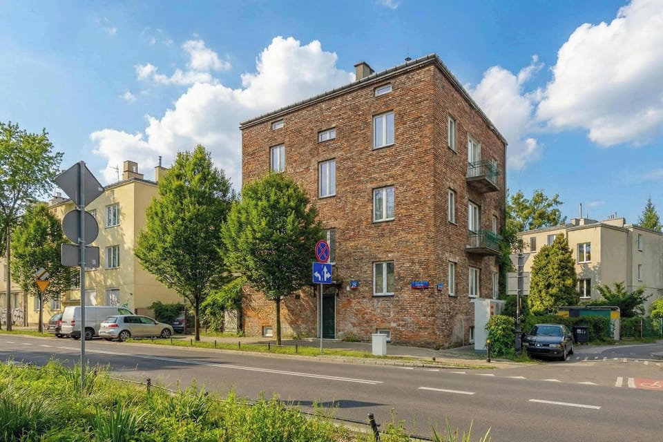 Building exterior shows a classic brick townhouse situated on a quiet, green corner.