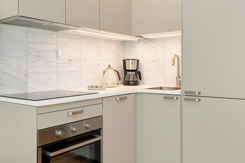 A close-up of the kitchen worktop with a built-in stovetop, oven, sink, and under-cabinet lighting. The neutral tones give a sleek, modern feel.