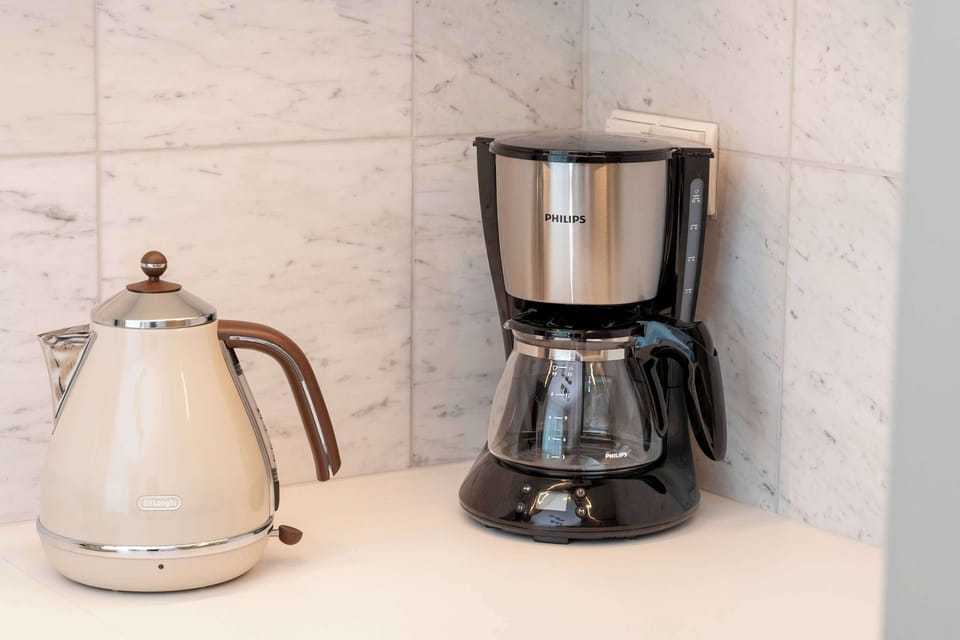 A countertop detail featuring a white electric kettle and a black drip coffee maker against a light marble backsplash. The arrangement suggests convenience for preparing hot drinks.