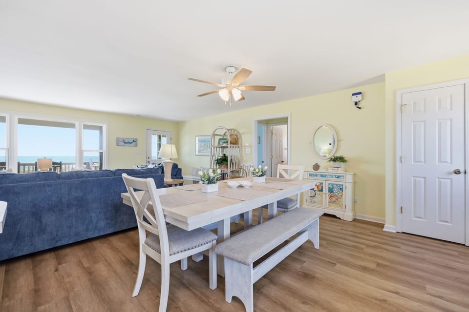 Step into your airy beach retreat where sunny yellow walls and coastal charm set the tone. Large windows frame stunning ocean views, perfect for morning coffee at your dining table or relaxing on the plush blue sofa.
