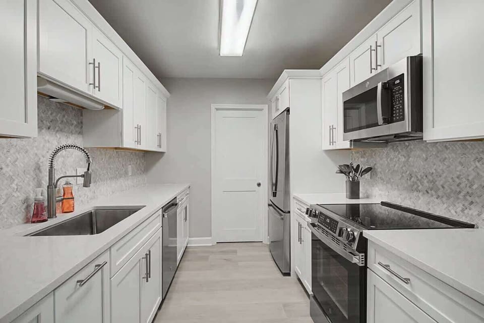 You'll love cooking in this pristine galley kitchen with sleek white cabinets, modern appliances, and elegant marble-pattern backsplash.