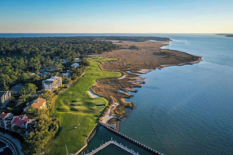 Stunning aerial view showcasing a premier coastal golf course with emerald fairways stretching to pristine waters and natural marshlands.
