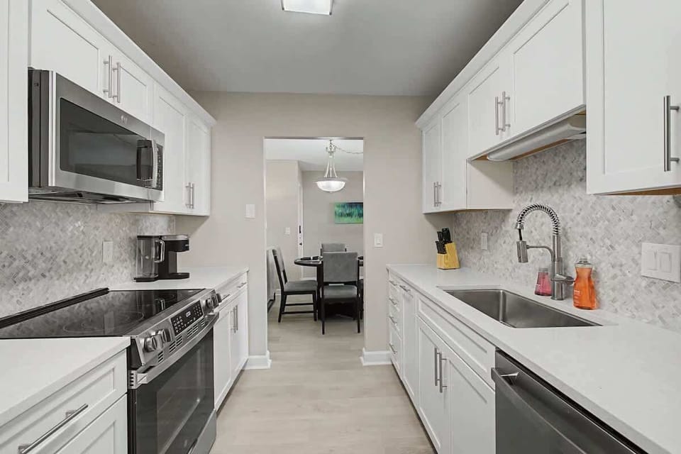 Your sleek galley kitchen features pristine white cabinets, marble backsplash, and stainless steel appliances—perfect for preparing memorable meals during your stay.