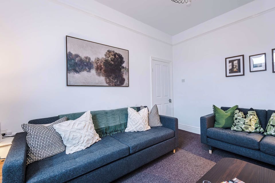 Living room with two modern gray sofas, a sleek wooden coffee table, and a matching TV stand. Includes side lamp, potted plant, and framed wall art,cozy, balanced space designed for relaxation and conversation in comfort.