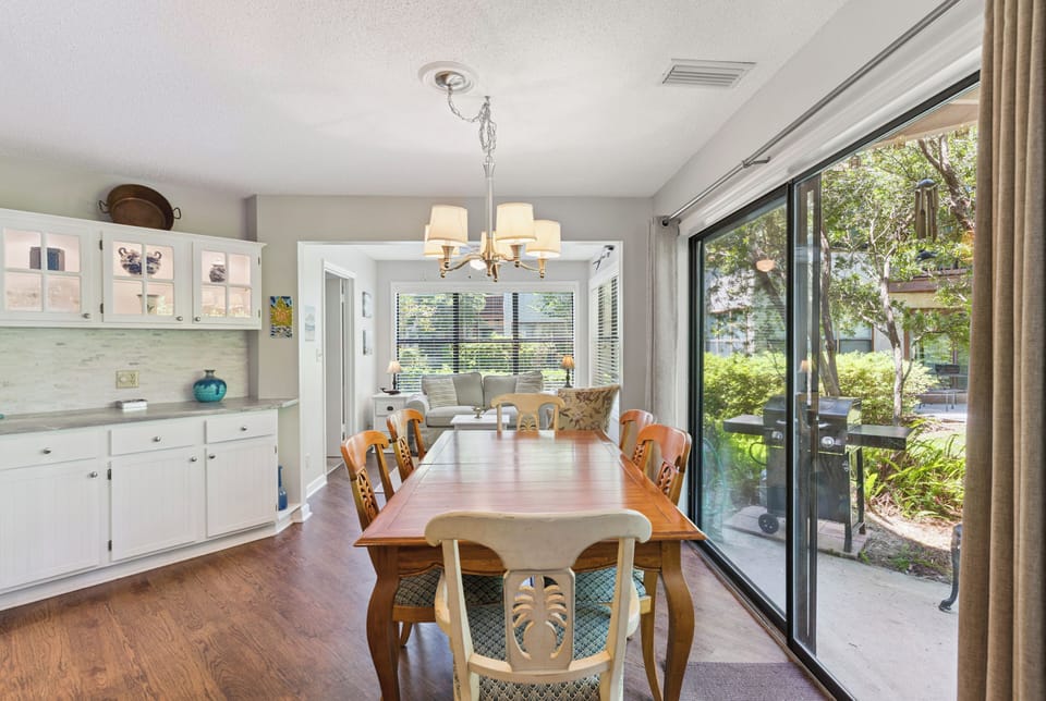 Gather around this warm dining table, with glass doors inviting the lush garden view inside and sunlight streaming through from every angle.