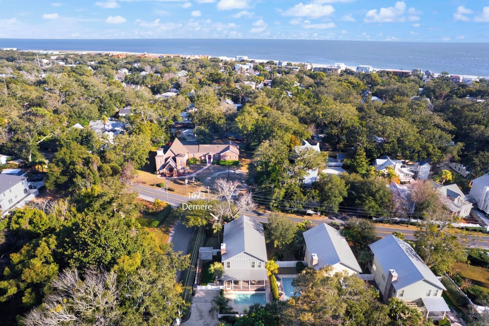 Aerial view of a coastal residential area with tree-lined streets leading to the ocean, showing the property's location within the peaceful neighborhood.