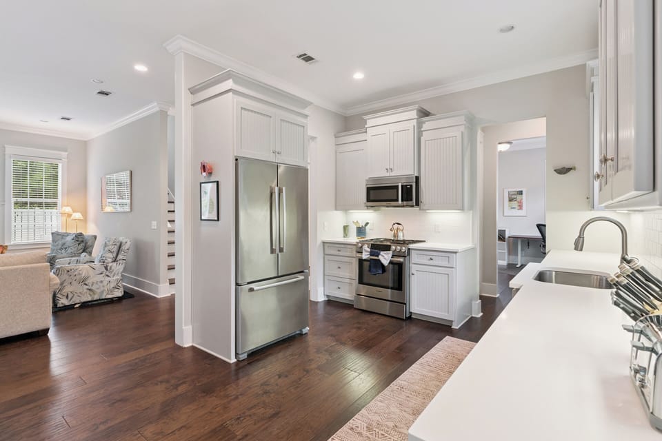 Step into your welcoming chef's space with pristine white cabinetry, gleaming stainless appliances, and rich hardwood beneath your feet—your perfect home away from home.