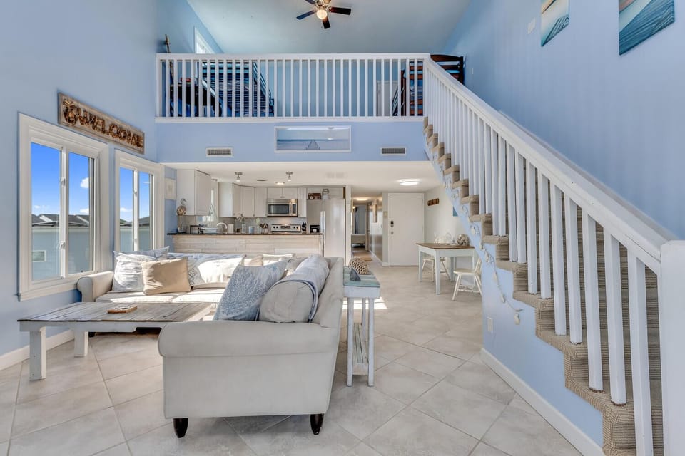 Relax in your bright, airy coastal living room with soaring ceilings, comfortable seating, and open kitchen for easy gathering.