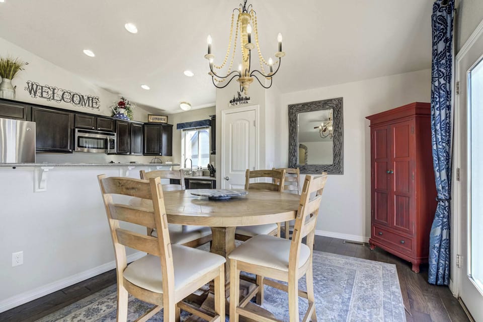 The functional kitchen and dining area features a wooden table with seating for four situated under a tiered chandelier. A raised breakfast bar provides additional counter space and a casual spot for quick meals or morning coffee.