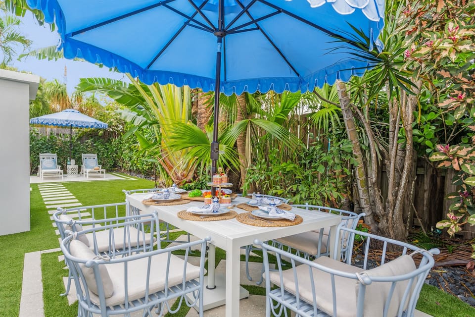 Enjoy open-air dining in a quiet garden corner, surrounded by tropical greenery and shaded by a bright umbrella.