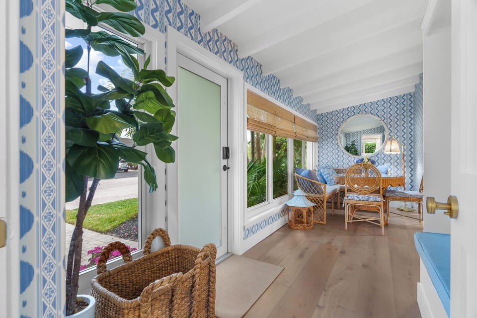 Relax and recharge in this bright sunroom featuring designer wallpaper, rattan seating, and views of the lush tropical landscaping.