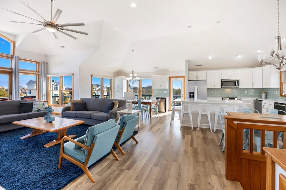 The open-concept top-level living area is filled with natural light from large windows and coastal-inspired décor.