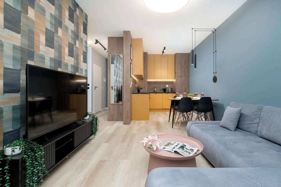 Another view of the living area looking toward the kitchen and dining space. The TV wall features multicolored rectangular tiles for a contemporary look. The open-plan layout connects the lounge and kitchen seamlessly.