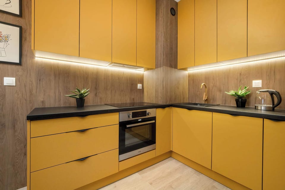 A kitchen with bold yellow cabinets and under-cabinet lighting. The countertops are dark, creating a strong contrast with the cabinetry. Built-in appliances are neatly integrated into the design.
