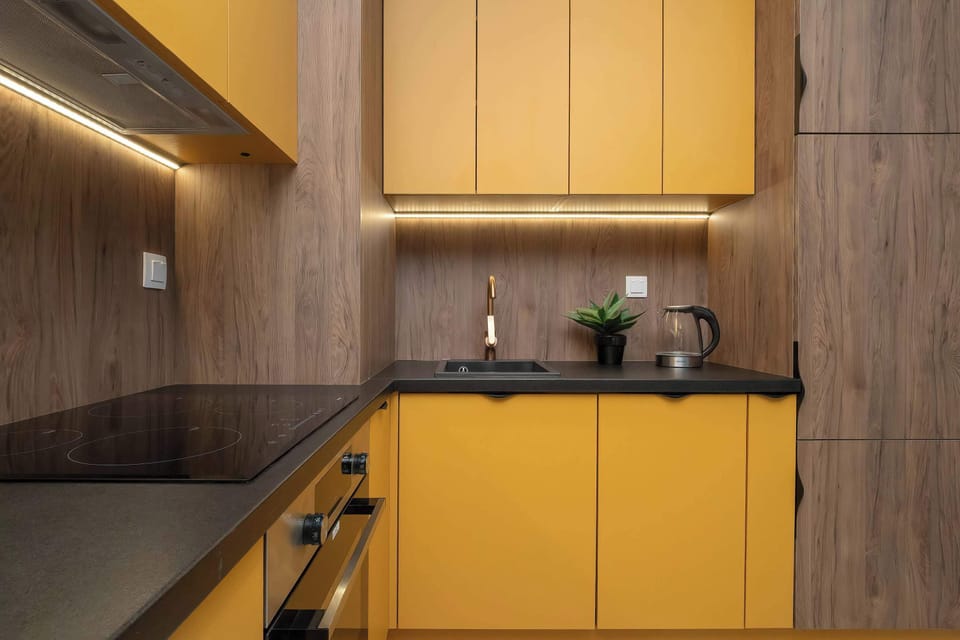 Another kitchen angle highlighting yellow cabinetry and dark countertops. Under-cabinet lighting illuminates the workspace. The layout appears functional and streamlined.