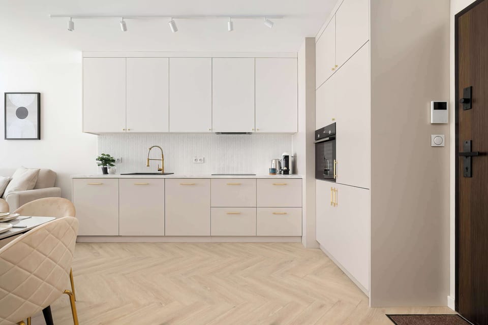 The elongated kitchenette boasts sleek, handle-less cream cabinets and a built-in oven, offering a professional space for meal preparation.