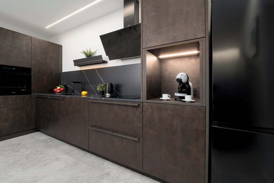A sleek, dark kitchen kitchenette is equipped with high-end built-in appliances and LED under-cabinet lighting.