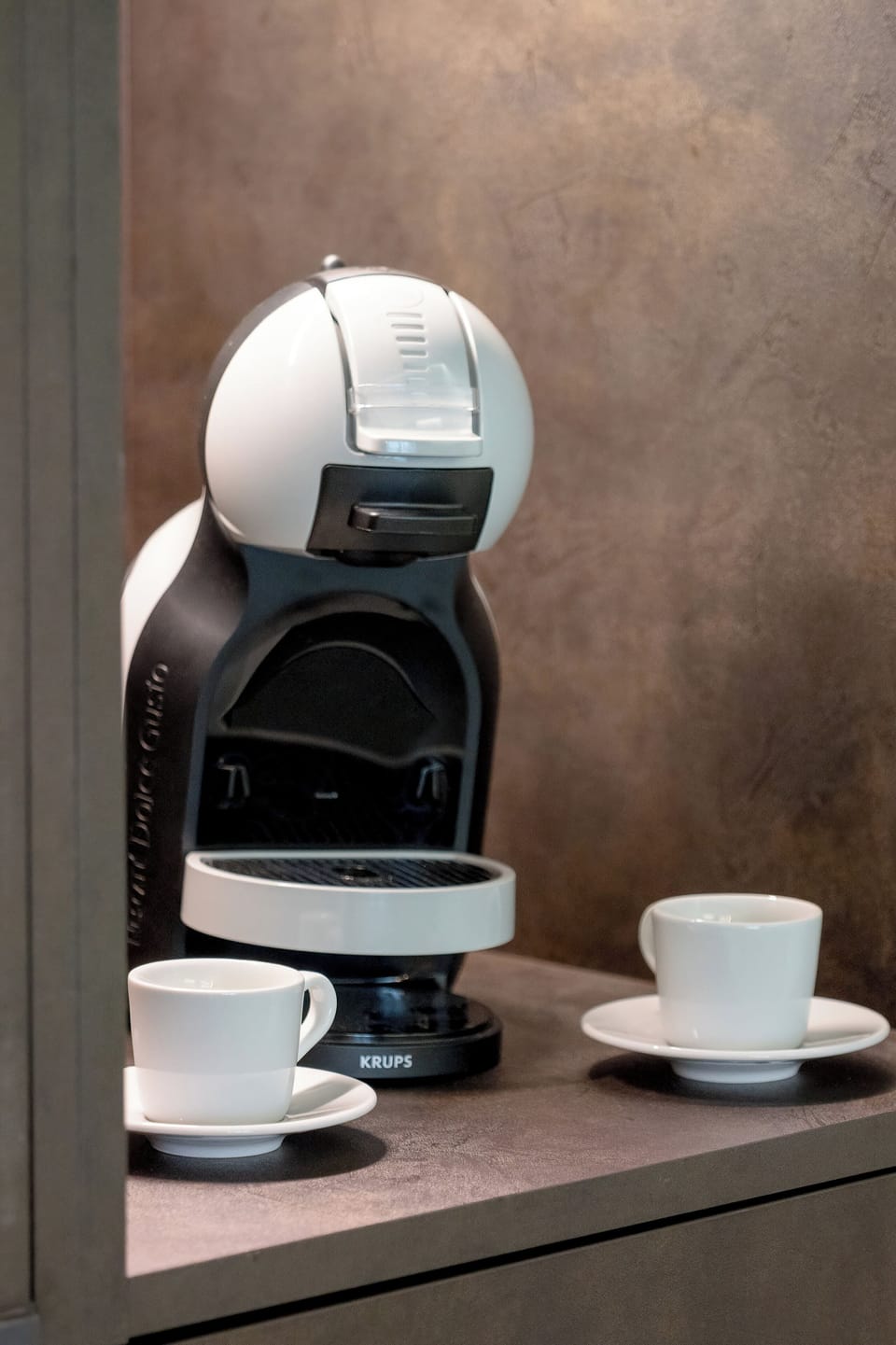 A modern capsule coffee machine stands ready on the kitchen counter, accompanied by two white ceramic cups.