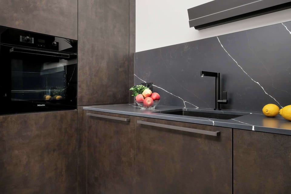 The kitchen workspace showcases a dark marble-patterned backsplash and a minimalist black faucet.