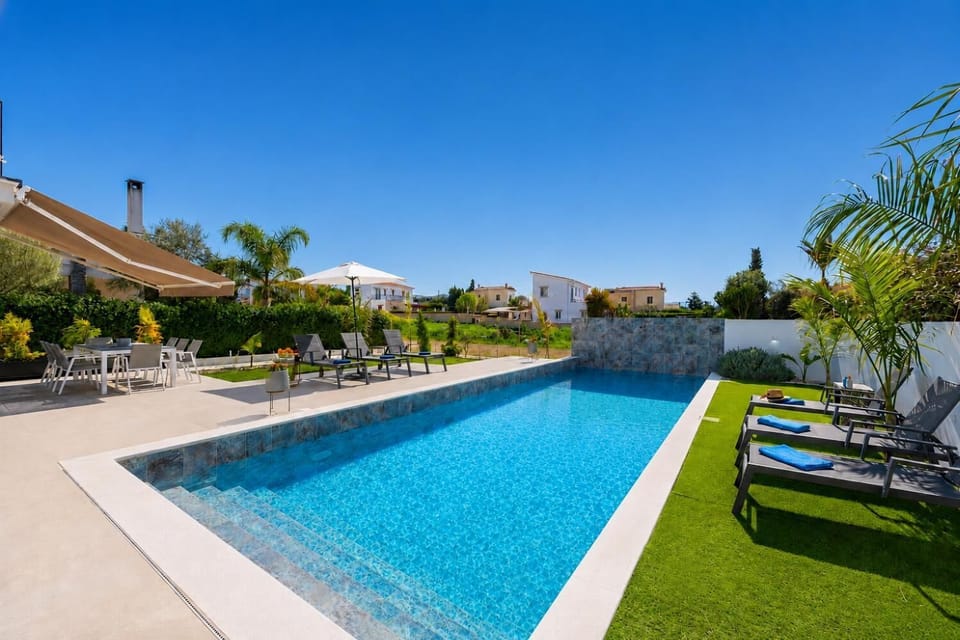 Sunny private pool area with modern loungers, shaded dining space, and a bright landscaped garden.