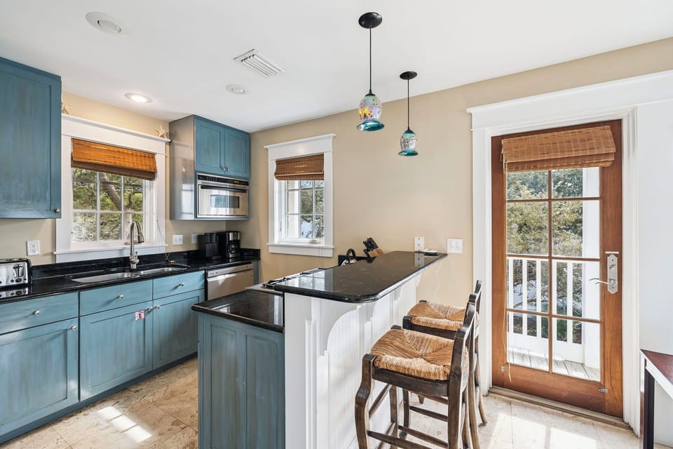 Your beautifully appointed kitchen awaits with blue cabinetry, granite counters, and charming pendant lights, perfect for your morning coffee.