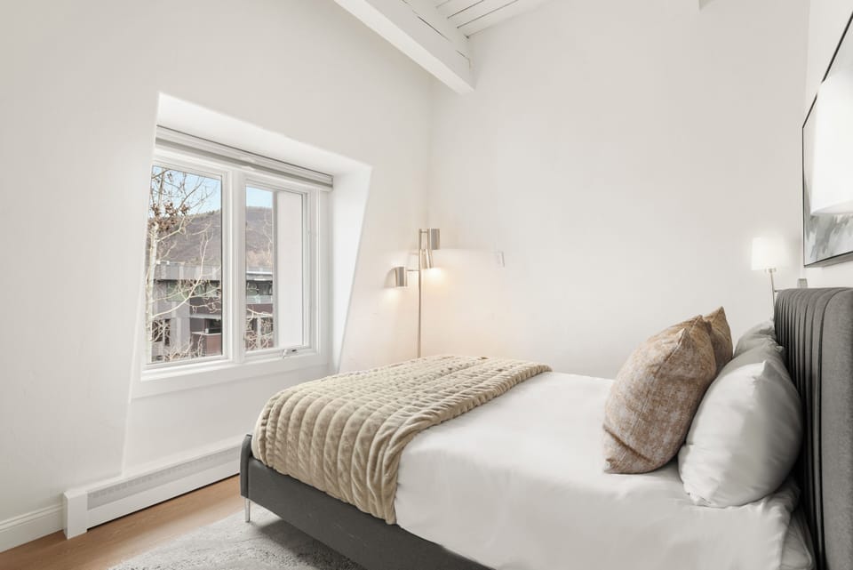 Guest bedroom with plush queen-sized bed, vaulted ceilings, 50" smart TV with Xfinity cable and Roku streaming, closet, dual light shades, mountain views, and shared hallway bathroom.